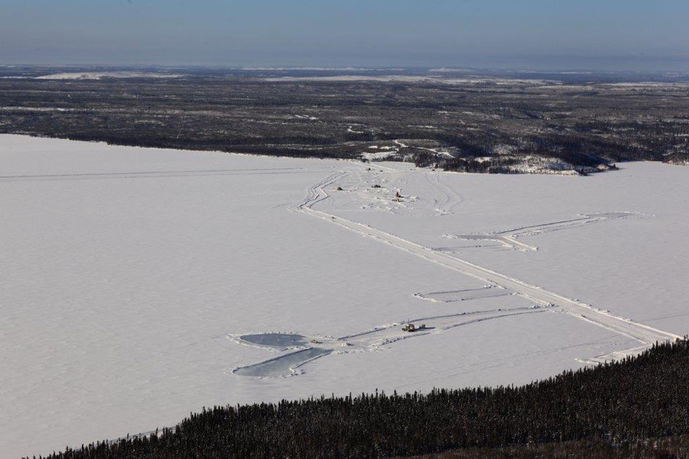 high altitude aerial of self made ice roads on frozen Canadian lake with snow covered ice and clearings of Bryson Drilling and diamond drilling equipment with distant heavy trees as far as the eye can see