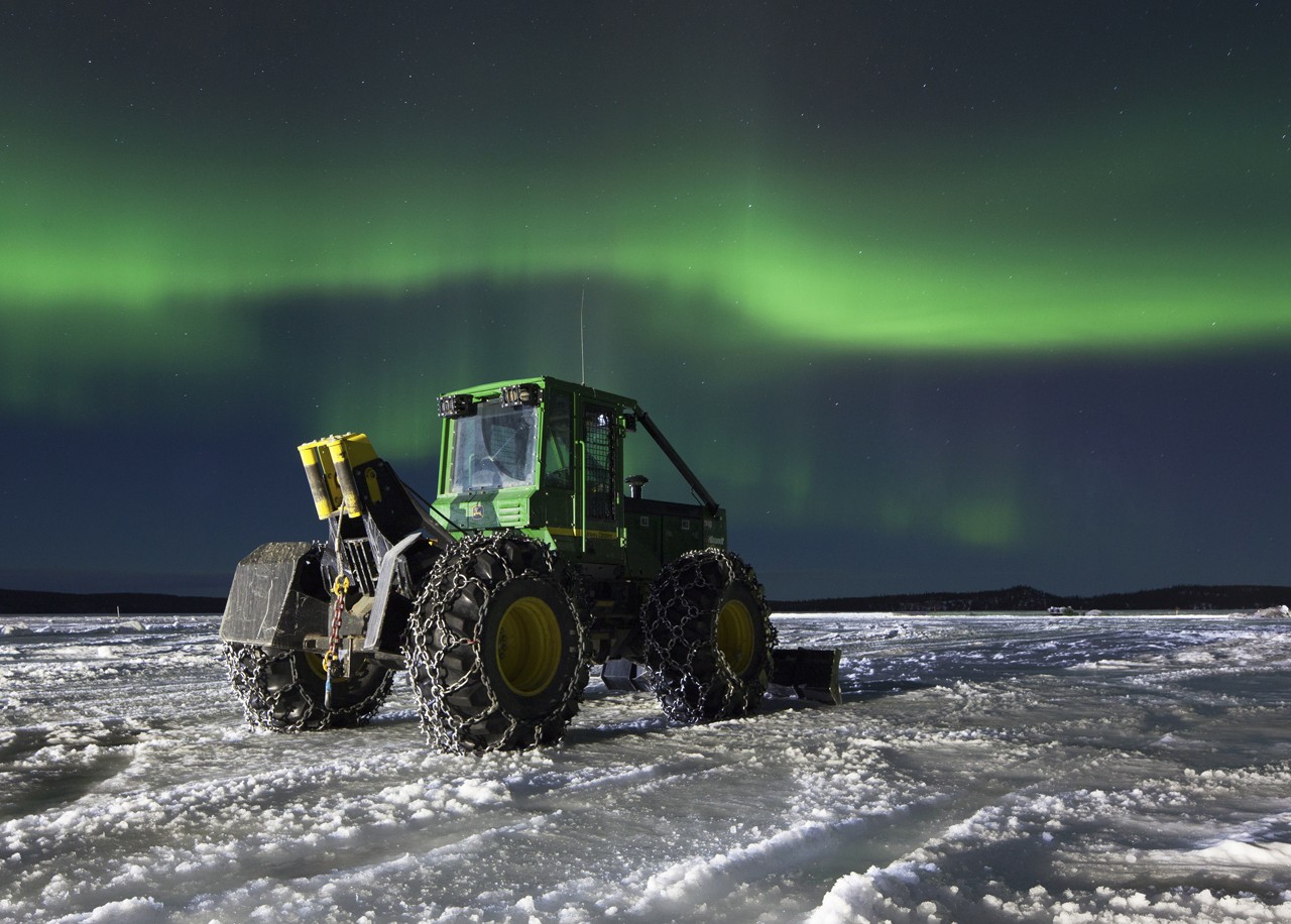 Bryson Drilling skid John Deer tractor on snowy ice with northern lights above on a night time diamond drill location