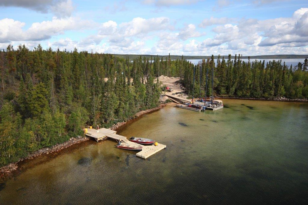 aerial view of forested lake shore marina with docks and a water barge is being setup with diamond drill equipment just off shore