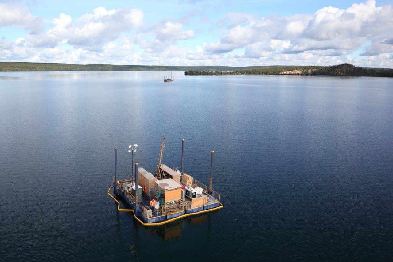 aerial view of two large floating diamond drill barges on a large lake with trees in the background